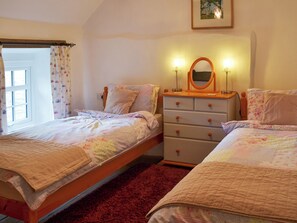A bedroom with two beds, a dresser with drawers, a mirror, and a window with curtains.
