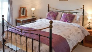 Ein Bett mit Metallgestell, ein Nachttisch, eine Lampe, ein Spiegel und ein Bild an der Wand.