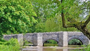 A stone bridge over a calm river, surrounded by lush greenery and trees. - Red Kite Cottage (Heyope, near Knighton)