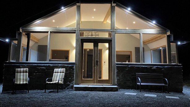 A modern house with a glass facade, a wooden door, and two chairs outside. - Red Kite Cottage (Heyope, near Knighton)