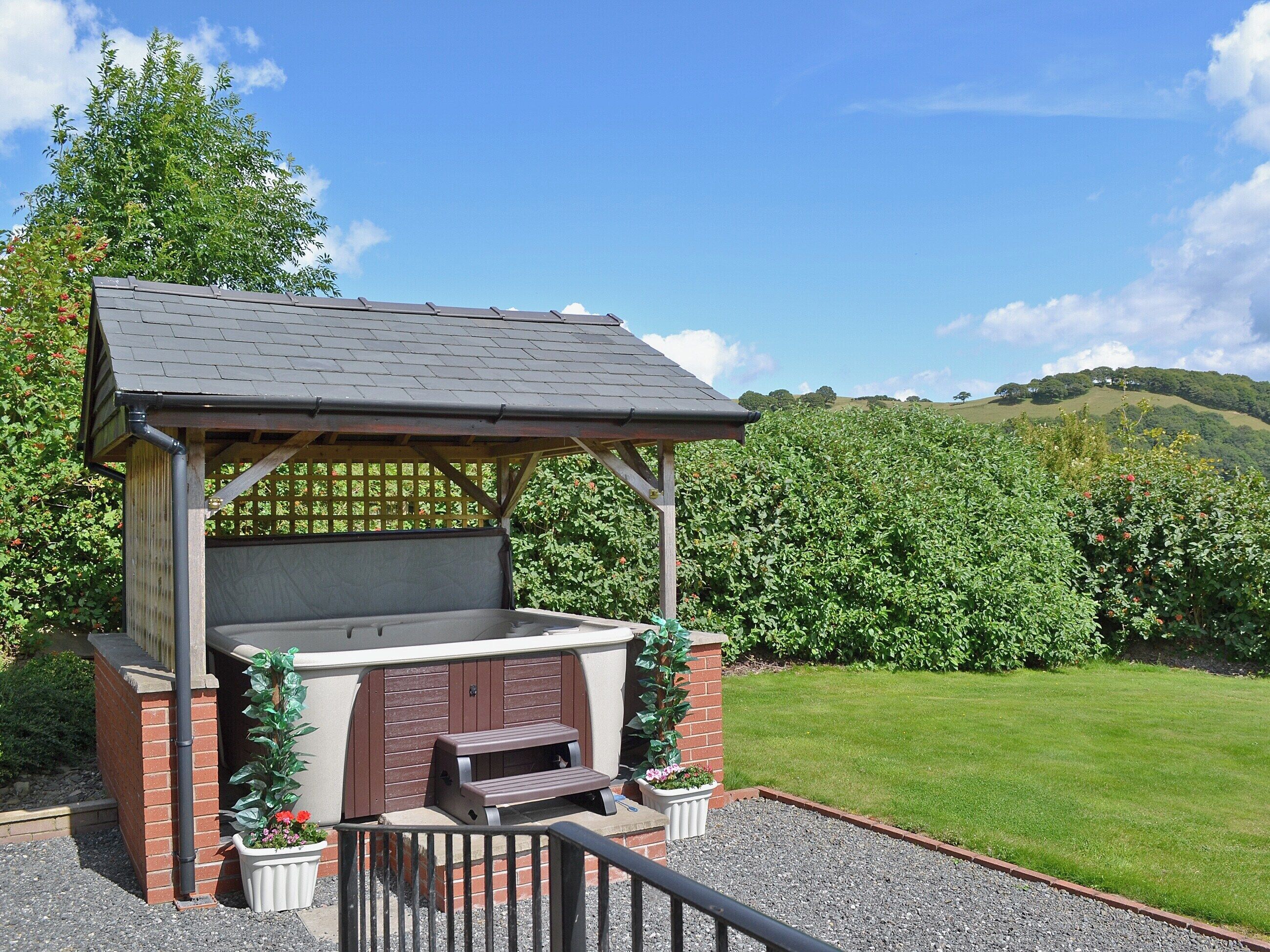 A gazebo with a bench and a small table, surrounded by a gravel area and a grassy lawn.