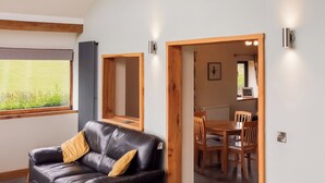 A modern living room with a black leather sofa, wooden sideboard, and a dining area with wooden chairs and a table. - Red Kite Cottage (Heyope, near Knighton)