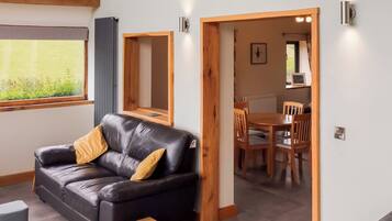 Un salon moderne avec un canapé en cuir noir, un buffet en bois et un coin repas comprenant des chaises et une table en bois.