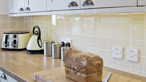 Een keuken met een brood op een houten snijplank, een broodrooster, een waterkoker en roestvrijstalen bakjes.