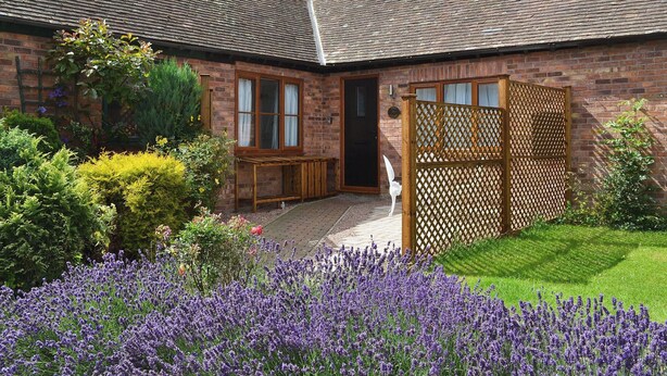 Een bakstenen huis met een pannendak, een houten hek en een tuin met lavendel.
