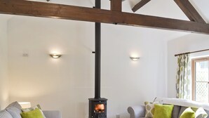 Een gezellige woonkamer met een open haard, twee banken met groene kussens en een raam met behangetjes.