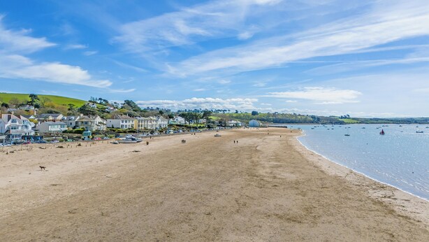 A wide sandy beach with houses in the background and boats in the water.