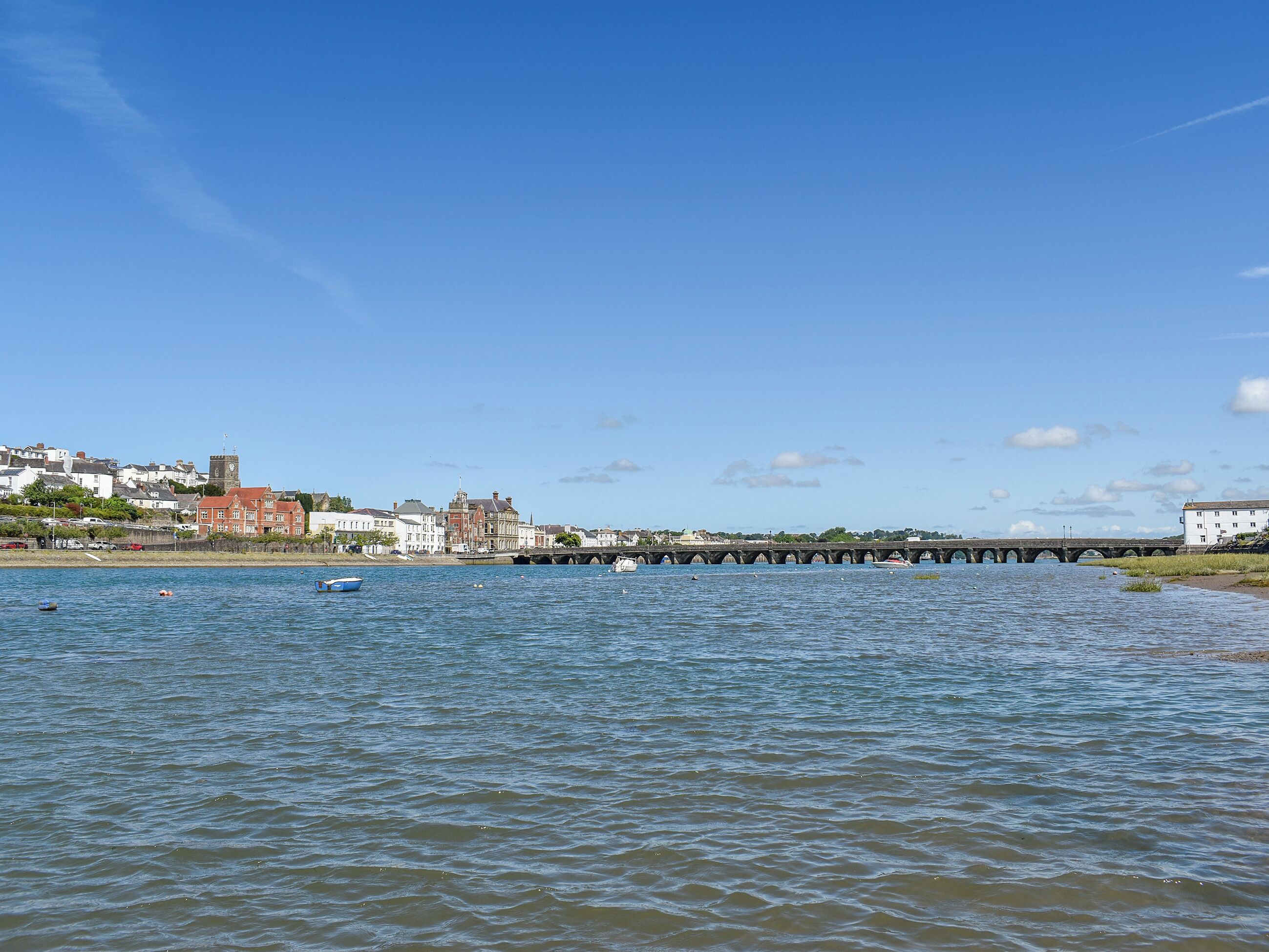 Une vue sur le bord de l’eau, avec un pont de pierre, des bâtiments et une eau calme.