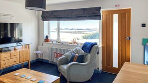 A modern living room with a television, wooden furniture, a comfortable armchair, and a view of a bridge.