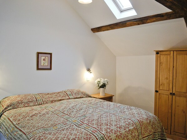 A bedroom with a large bed, a wooden wardrobe, a small table with a vase of flowers, a framed picture on the wall, and a skylight. - 2 bedroom accommodation in Ashperton, near Ledbury (Ashperton, near Ledbury)
