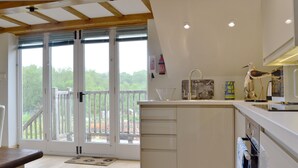 A kitchen with a wooden floor, white cabinets, a sink, and a view through glass doors to an outdoor balcony. - 1 bedroom accommodation in Upper Brailes, near Banbury (Upper Brailes, near Banbury)