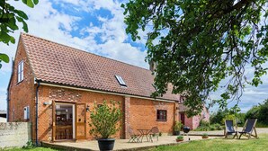 Une maison en briques avec un toit en tuiles, une porte d’entrée et un petit porche aménagé avec du mobilier d’extérieur.