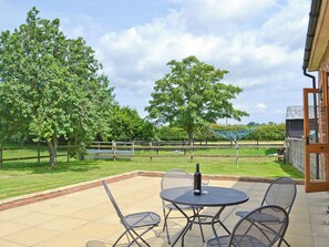 An outdoor patio with a table and chairs, a bottle, and a wine glass. - 2 bedroom accommodation in Aldeby, near Beccles (Aldeby, near Beccles)