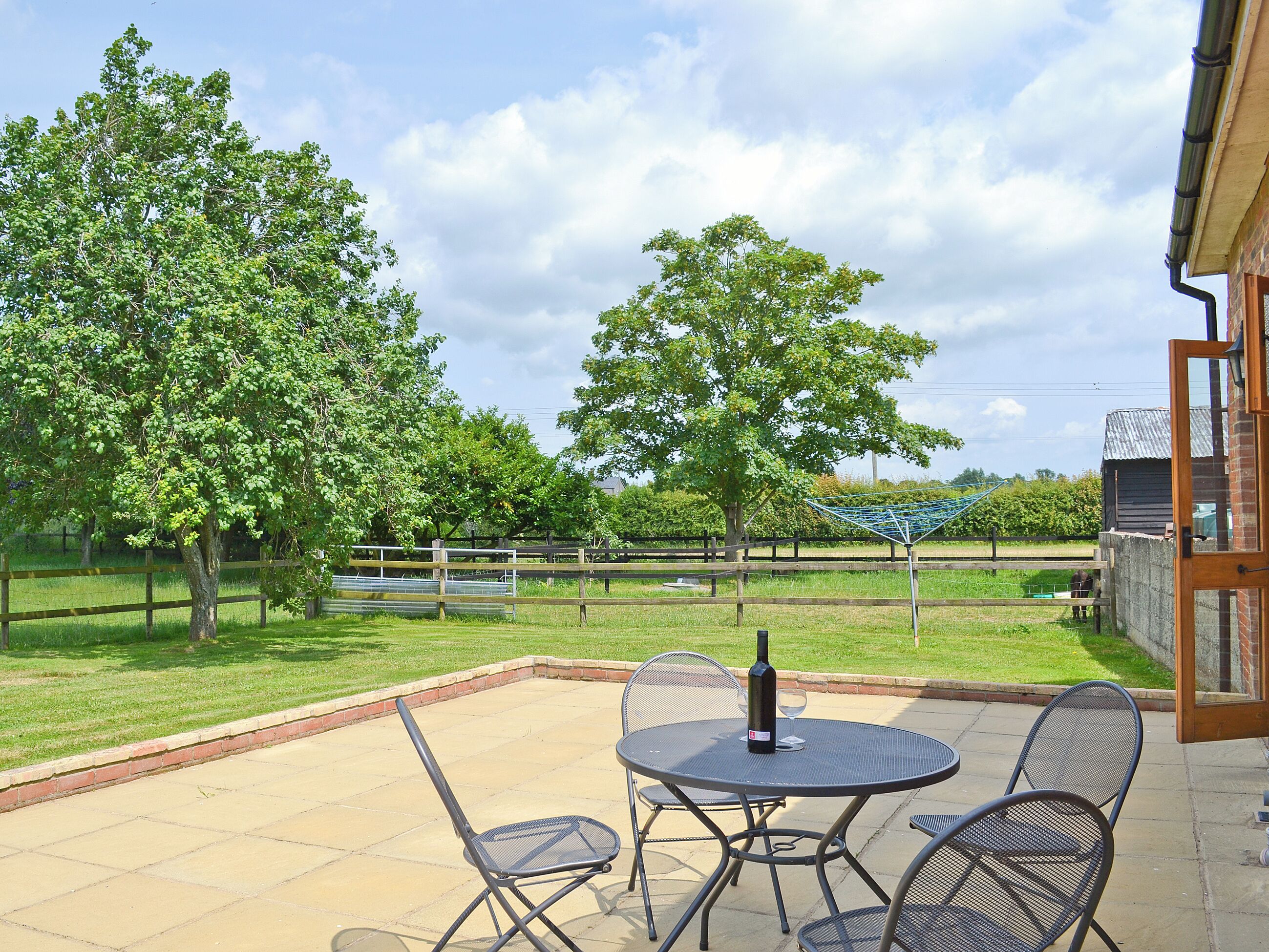 An outdoor patio with a table and chairs, a bottle, and a wine glass.