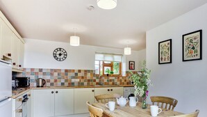 Une cuisine avec des meubles blancs, un pare-feu en carrelage et une table à manger en bois, accompagnée de chaises.