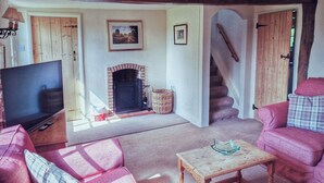 Ein gemütliches Wohnzimmer mit Kamin, Fernseher und einer Treppe, die zu einer weiteren Ebene führt.