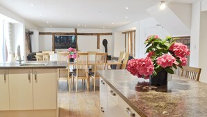 A modern kitchen with wooden cabinets, a granite countertop, and a dining area with wooden chairs and a table. - 5 bedroom accommodation in Botesdale, near Diss (Botesdale, near Diss)