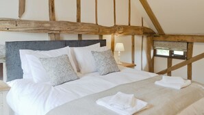 A bed with white linens, patterned pillows, and a folded towel. The room features exposed wooden beams and a simple nightstand with a lamp. - 5 bedroom accommodation in Botesdale, near Diss (Botesdale, near Diss)