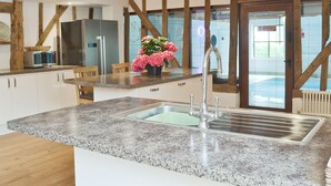 A modern kitchen with granite countertops, a stainless steel sink, wooden beams, and a view of the outside. - 5 bedroom accommodation in Botesdale, near Diss (Botesdale, near Diss)