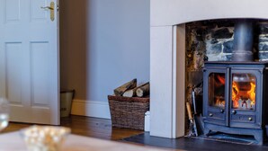 A room with a wood-burning stove, a white door, and a basket of firewood. - 3 bedroom accommodation in Hartland, near Bideford (Hartland, near Bideford)