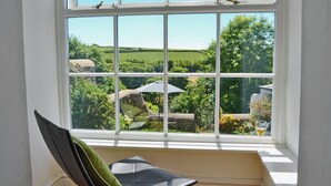 A room with a large window overlooking a garden, a chair, and a table with a glass. - 3 bedroom accommodation in Hartland, near Bideford (Hartland, near Bideford)