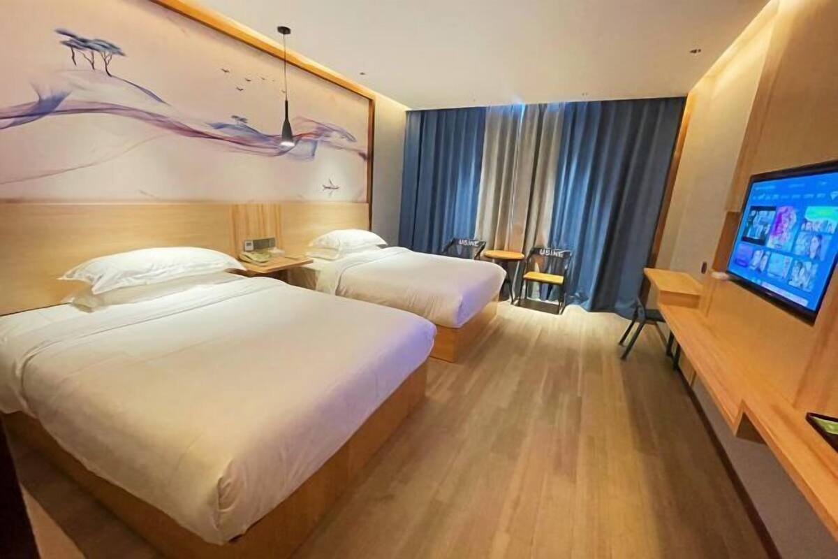 Hotellihuone, jossa on kaksi sänkyä, televisio, työpöytä ja tuoli.