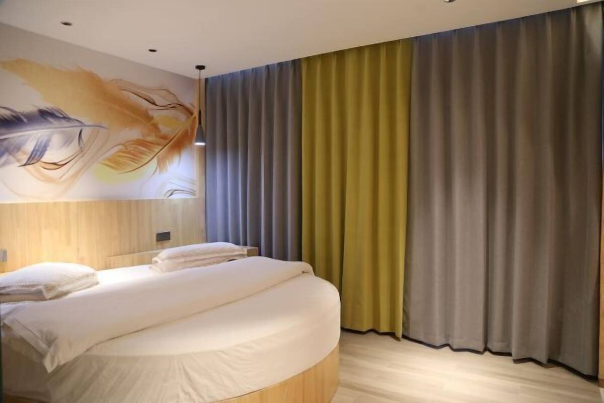 Moderni hotellihuone, jossa on kaareva sänky, suuri taulu seinällä ja näkymä kaupunkiin ikkunasta.