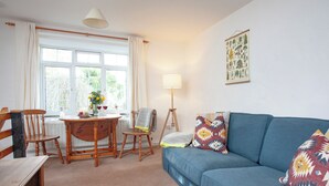 A cozy living room with a blue sofa, wooden chairs, a dining table with a vase of flowers, and a lamp. - 2 bedroom accommodation in Looe (Looe)
