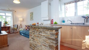 A kitchen with a stone island, wooden cabinets, and a window with a view of greenery. - 2 bedroom accommodation in Looe (Looe)