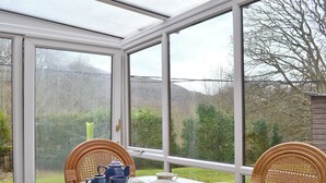 Une véranda avec une table dressée pour le thé, des chaises en osier et une vue sur un jardin et des collines.