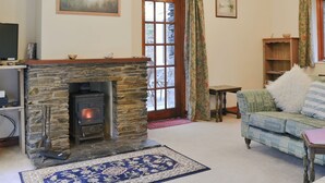 Un salon chaleureux avec une cheminée en pierre, un téléviseur posé sur une étagère, un canapé et un tapis à motifs.