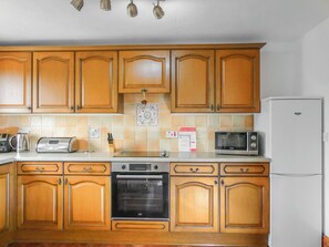 A kitchen with wooden cabinets, a toaster, a kettle, a microwave, a stove, and a refrigerator.