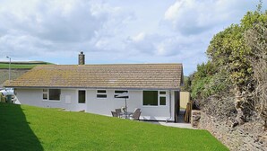 A single-story house with a sloped roof, a chimney, and a small patio area with outdoor furniture. - 2 bedroom accommodation in Port Isaac (Port Isaac)