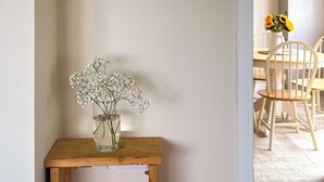 A wooden table with a clear glass vase containing white flowers, positioned against a plain wall. - 2 bedroom accommodation in Port Isaac (Port Isaac)