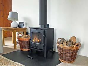 A room with a black wood-burning stove, two wicker baskets filled with firewood, a lamp on a wooden table, and a rug on the floor. - 2 bedroom accommodation in Wadhurst, near Tunbridge Wells (Wadhurst, near Tunbridge Wells)