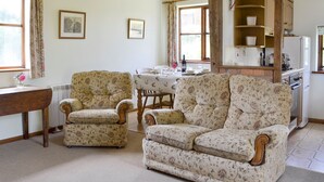 A cozy living room with floral-patterned armchairs, a wooden dining table, and a kitchen area with a refrigerator and cabinets. - 2 bedroom accommodation in Wadhurst, near Tunbridge Wells (Wadhurst, near Tunbridge Wells)