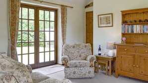 A cozy room with a floral-patterned sofa, a wooden cabinet with books, and a window with curtains. - 2 bedroom accommodation in Wadhurst, near Tunbridge Wells (Wadhurst, near Tunbridge Wells)