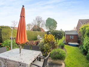 Un jardin avec une table et des chaises, un abri en bois et une haie.