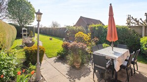 A patio area with a table and chairs, surrounded by a well-maintained garden and a hedge. - 3 bedroom accommodation in Ringstead, near Hunstanton (Ringstead, near Hunstanton)