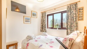 A bedroom with a bed, a bedside table, a window with curtains, and a wall-mounted television. - 3 bedroom accommodation in Ringstead, near Hunstanton (Ringstead, near Hunstanton)