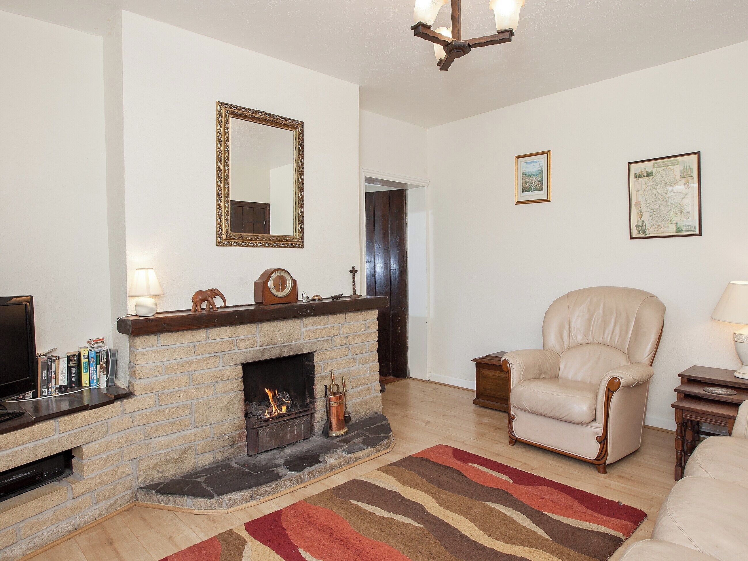 A living room with a fireplace, a leather armchair, a television, and a bookshelf.