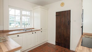 A kitchen with white cabinets, a wooden countertop, a dark wooden door, and a window with a view of greenery outside. - 4 bedroom accommodation in Chatcull, near Eccleshall (Chatcull, near Eccleshall)