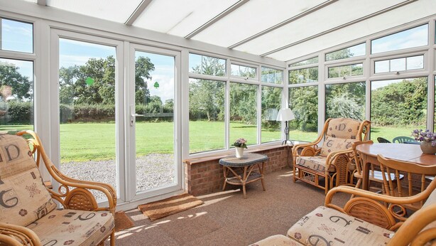 A conservatory with wicker furniture, a brick wall, and a view of a green garden. - 4 bedroom accommodation in Chatcull, near Eccleshall (Chatcull, near Eccleshall)