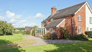 A large brick house with a conservatory, surrounded by a well-maintained lawn and a gravel path. - 4 bedroom accommodation in Chatcull, near Eccleshall (Chatcull, near Eccleshall)