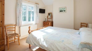 A bedroom with a bed, a wooden chair, a dresser, a television, and a window with curtains. - 4 bedroom accommodation in Chatcull, near Eccleshall (Chatcull, near Eccleshall)