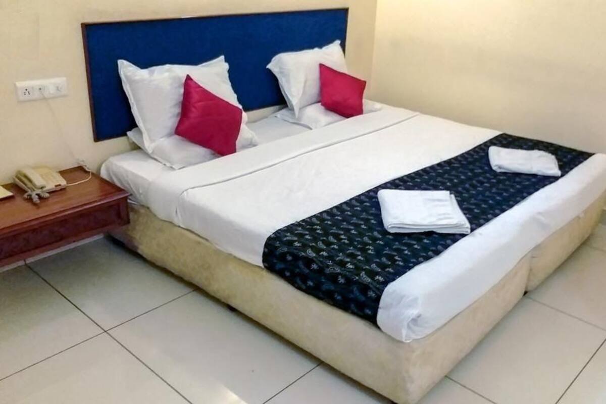 Cama bem arrumada com almofadas brancas e vermelhas, cabeceira azul e mesa de cabeceira com telefone.