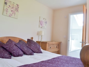 A bedroom with a bed, a nightstand, a lamp, and a door leading to a balcony.