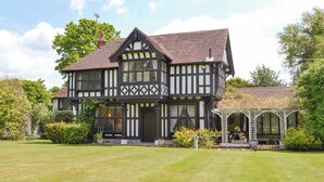 A Tudor-style house with a symmetrical facade, multiple windows, and a well-maintained lawn. - 3 bedroom accommodation in Little Chart, near Ashford (Little Chart, near Ashford)