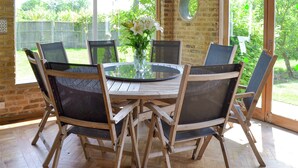 A round wooden table with six chairs, a glass top, and a vase with flowers. - 3 bedroom accommodation in Little Chart, near Ashford (Little Chart, near Ashford)