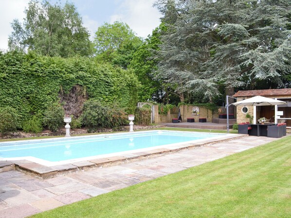 Une piscine rectangulaire bordée de pierres, entourée d’une pelouse bien entretenue et d’une végétation luxuriante.